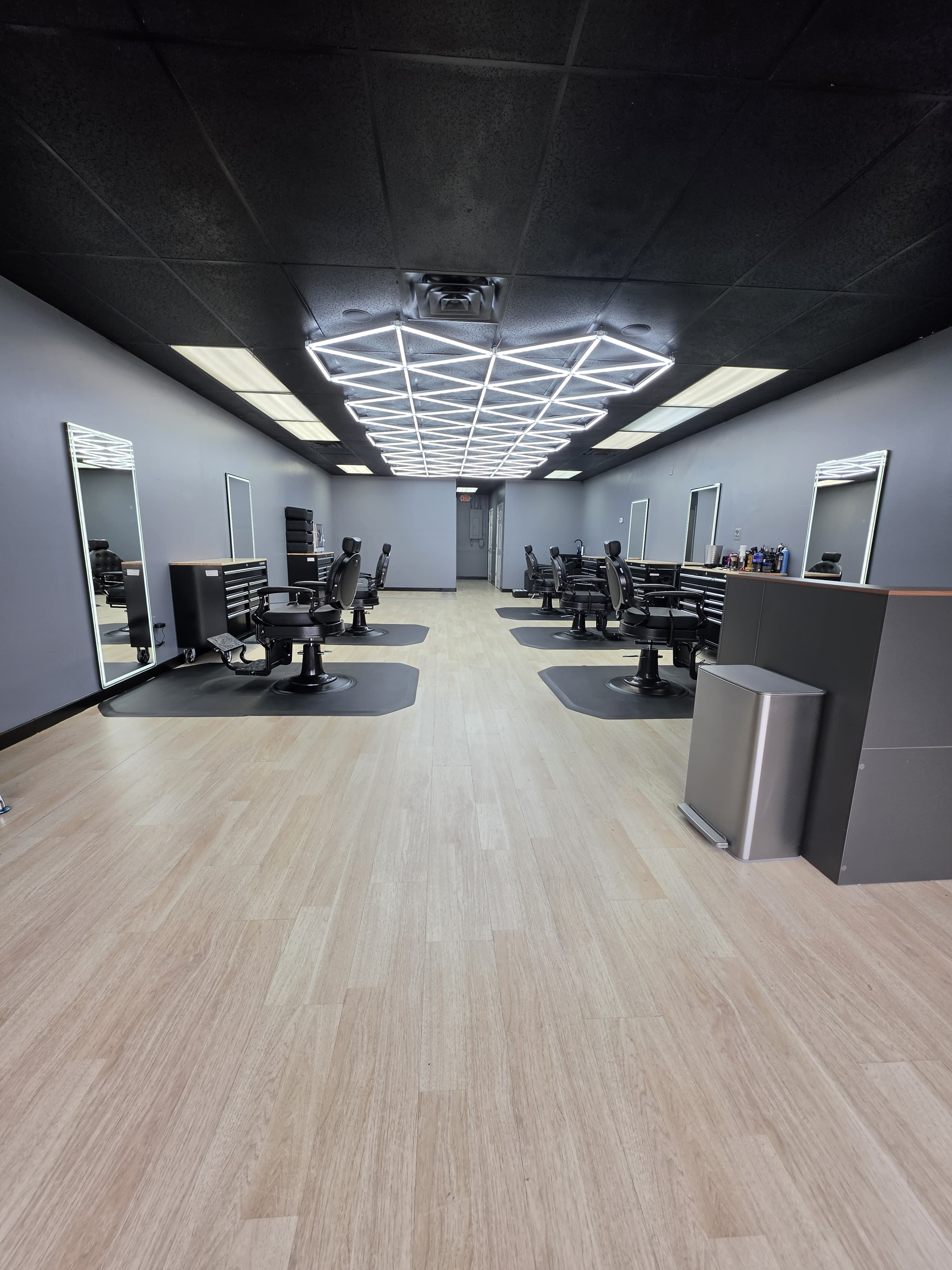 Symmetric view of the barbershop floor with paired barber chairs and mirrors along both walls under a geometric LED ceiling light