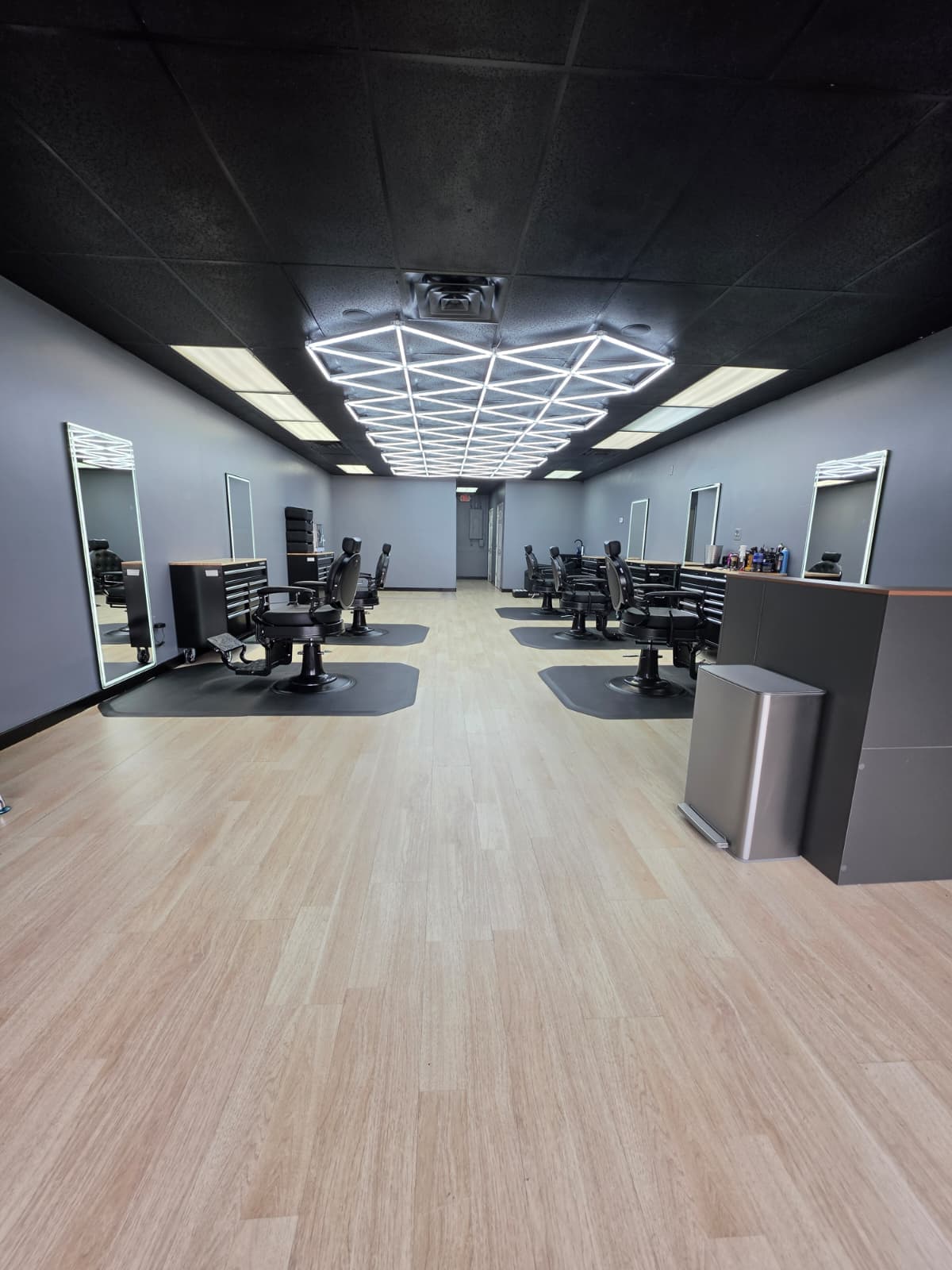 Barber chairs and lighted mirrors along the wall beneath the diamond LED ceiling fixture